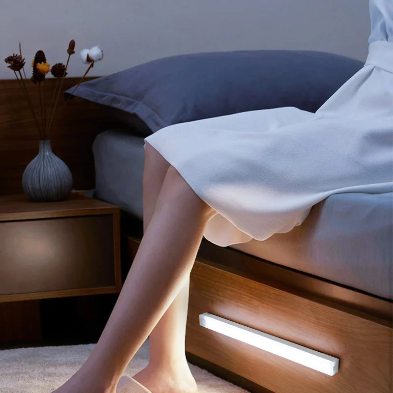 A person is sitting on a wooden bed with a bright LED bar light illuminating the bedside area.