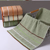 A set of stacked bath towels in earthy tones including beige, olive green, and terracotta.