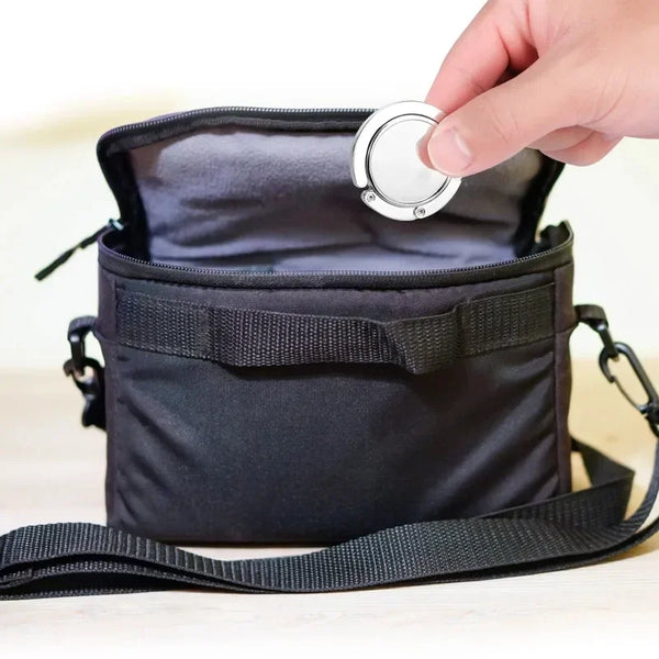 Una mano abre una bolsa plegable negra con un gancho de cierre plateado.