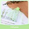 A light green organza drawstring gift bag filled with dried greenery, resting on a wooden surface.