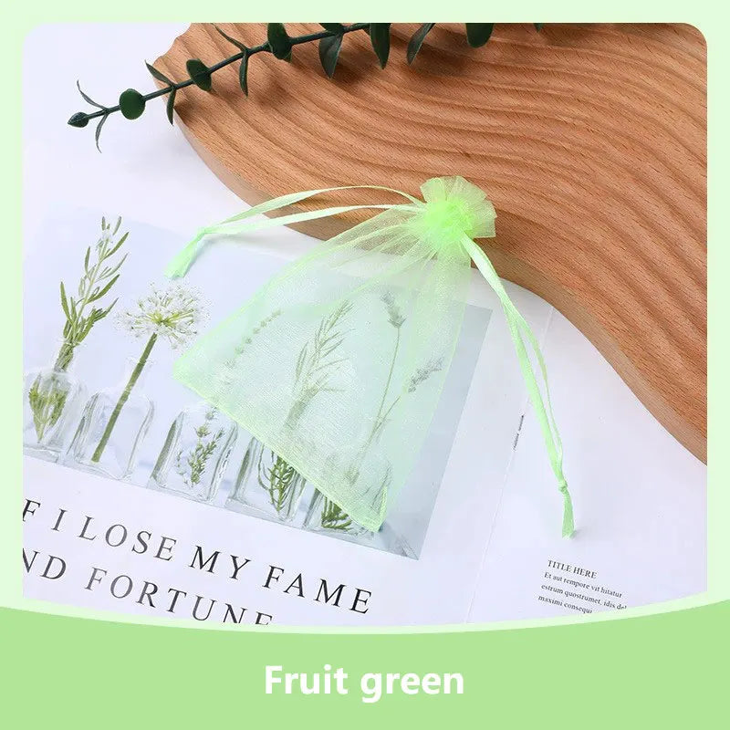 A light green organza drawstring gift bag filled with dried greenery, resting on a wooden surface.