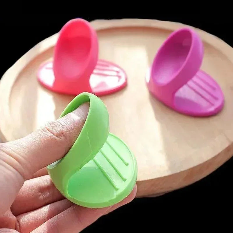 A hand holds a bright green silicone finger cover for baking and cooking on a wooden board.
