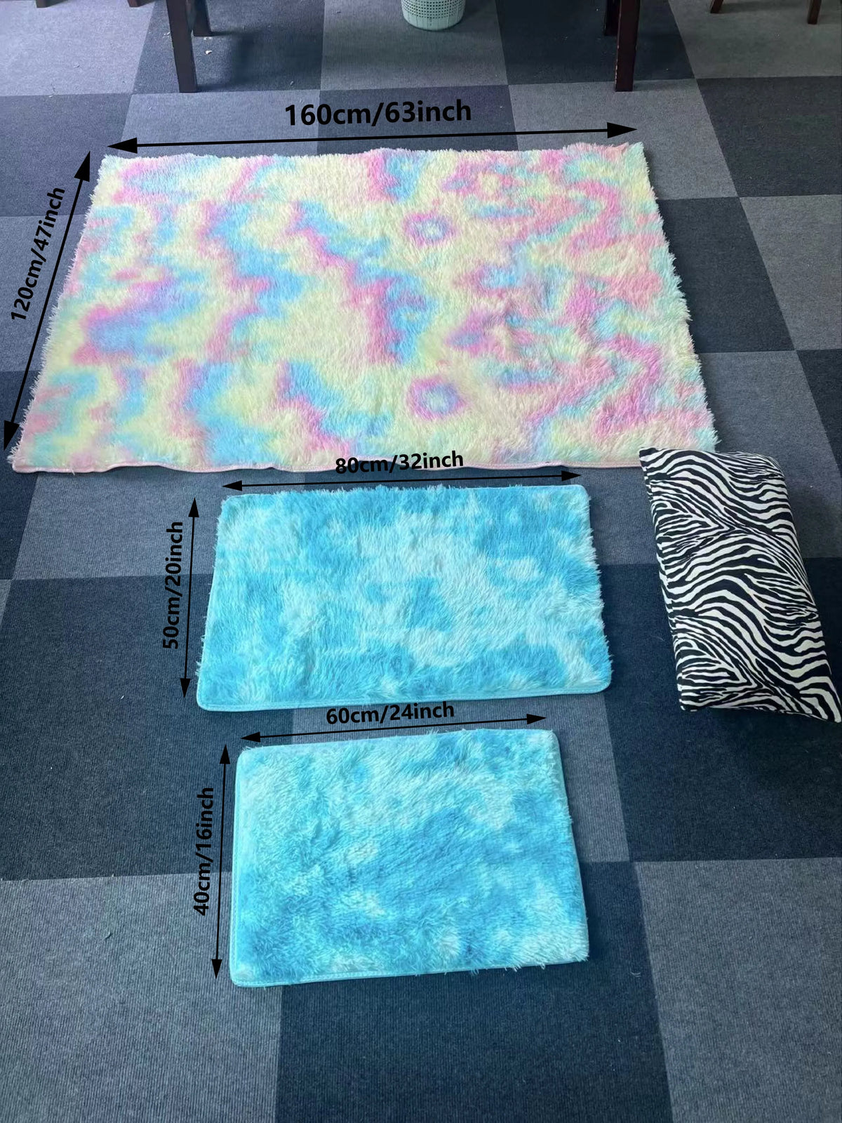 Three plush silk-touch area rugs in pastel colors and black zebra pattern displayed on a gray tiled floor.