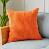 An orange ribbed corduroy cushion cover placed on a gray sofa next to a potted plant.