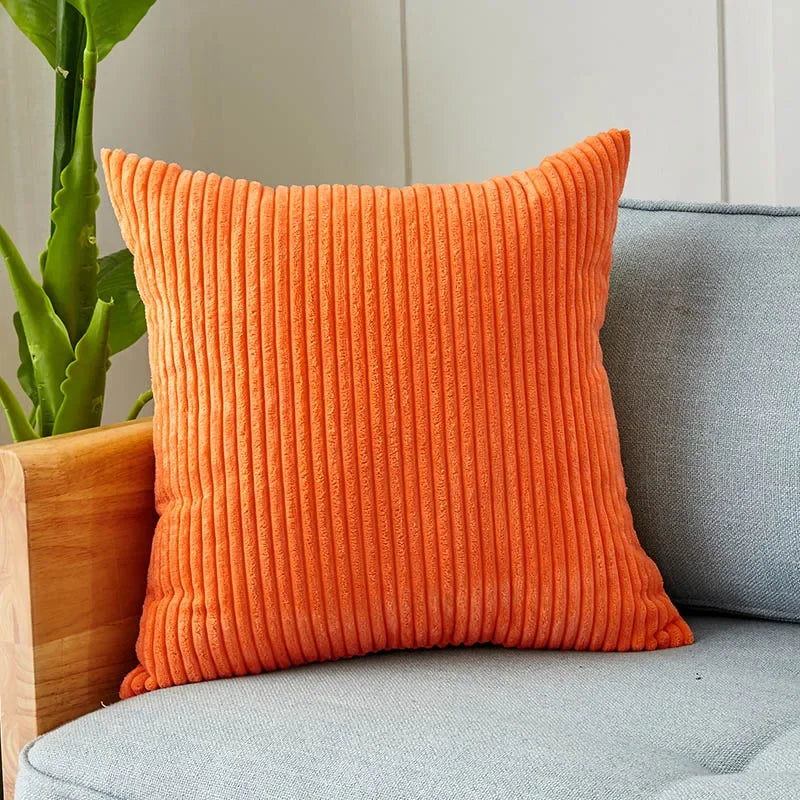 An orange ribbed corduroy cushion cover placed on a gray sofa next to a potted plant.