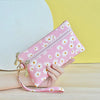 A hand holds a pink daisy print PU leather wristlet wallet with a zipper closure against a yellow background.