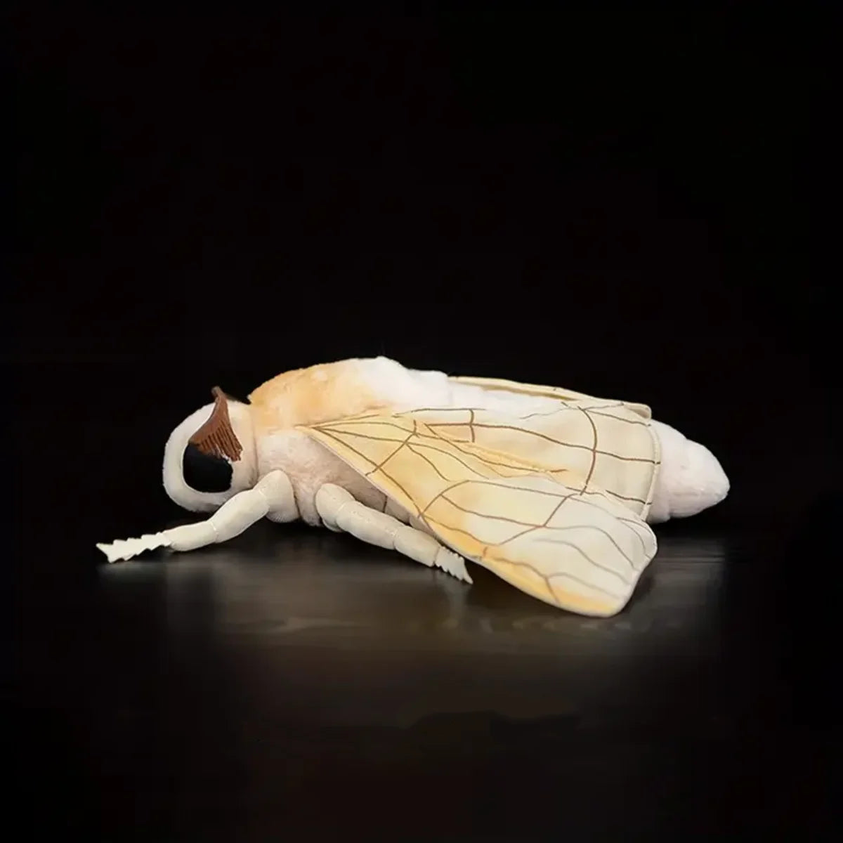 A soft and cuddly plush toy of a Luna moth with pale yellow wings and body against a dark background.