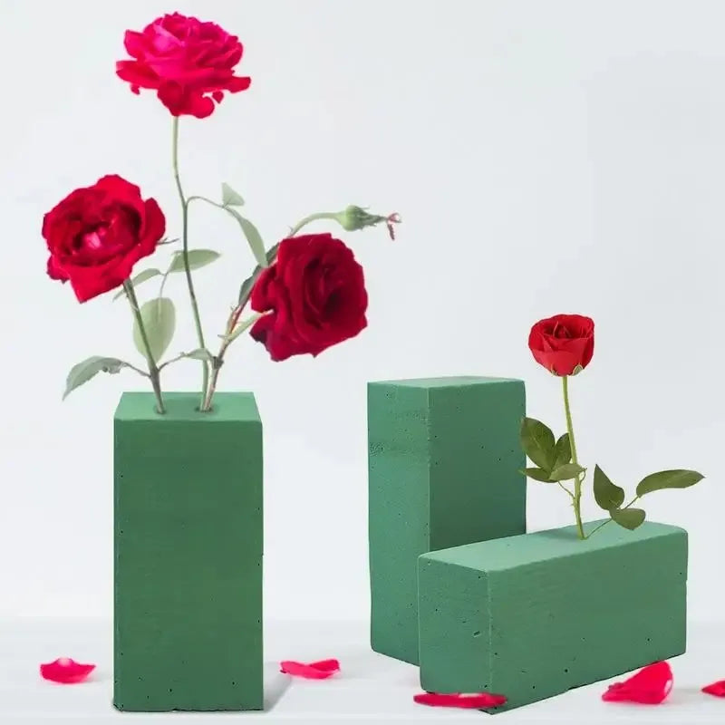A vibrant red rose in a square green foam block with a green stem and leaves.