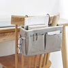A gray hanging storage organizer with cotton pockets is displayed on a wooden desk.