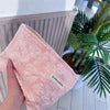 A pink canvas charger storage pouch is being held, with a green tropical plant in the background.
