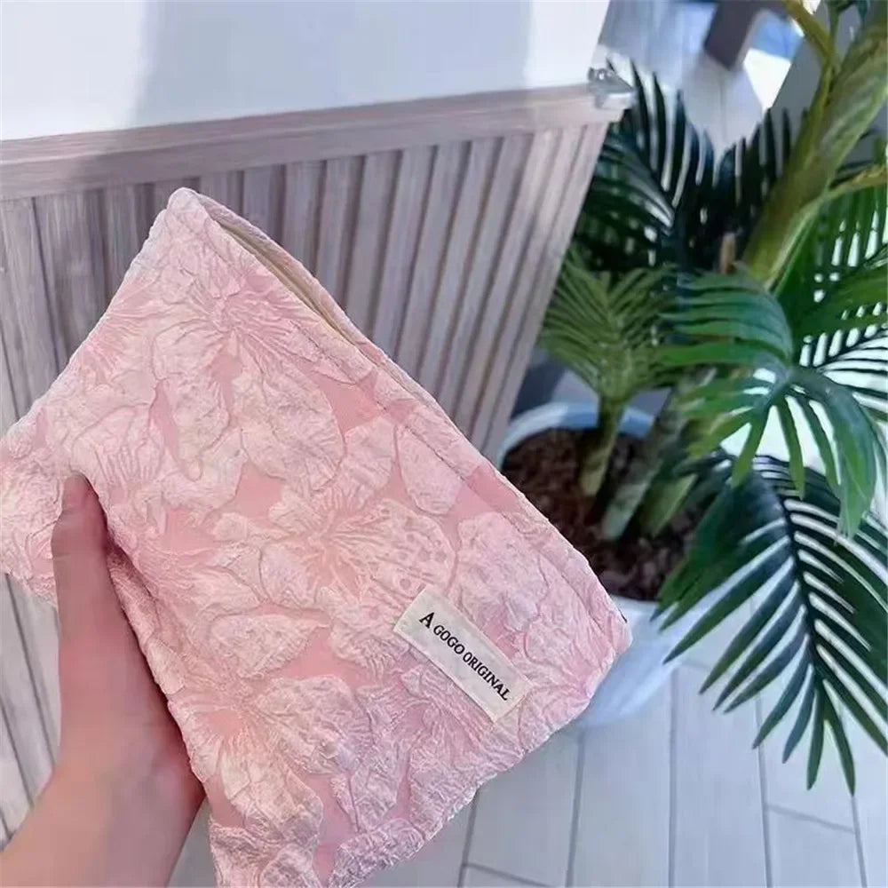 A pink canvas charger storage pouch is being held, with a green tropical plant in the background.