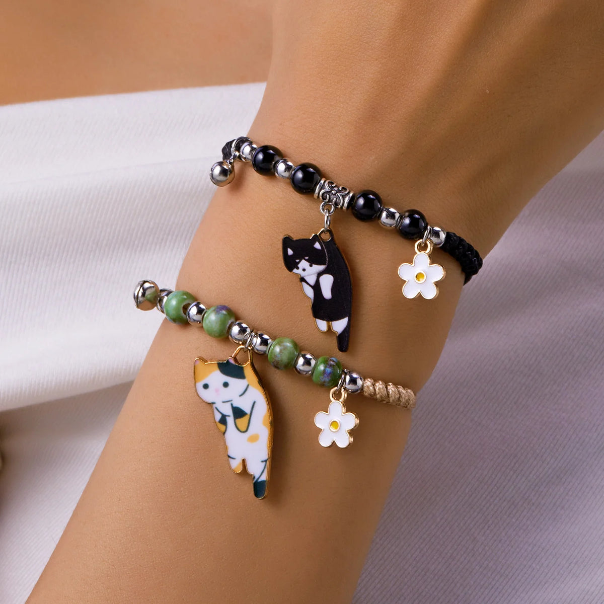 Armband mit Emaille-Anhänger einer schwarzen und einer weißen Katze sowie kleinen Blumenanhängern.