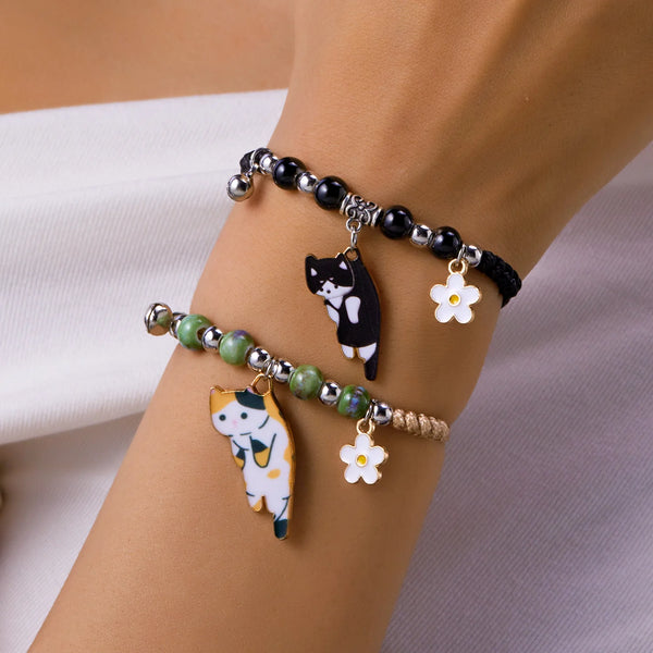 A bracelet featuring enamel charms of a black cat and a white cat, along with small flower charms.