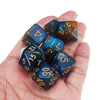 A hand holds a set of seven multicolor polyhedral dice for tabletop role-playing games