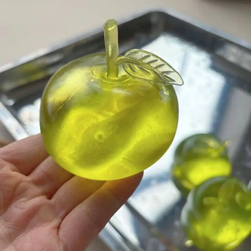 A hand holds a yellow, fruit-shaped squeeze toy with a leaf on top.