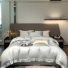 Luxuriöses Bett mit silberner Bettwäsche und Kissen vor neutraler Wand in einem modernen Schlafzimmer.