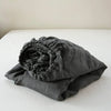 A dark gray linen fitted sheet with deep pockets is folded on a white surface.
