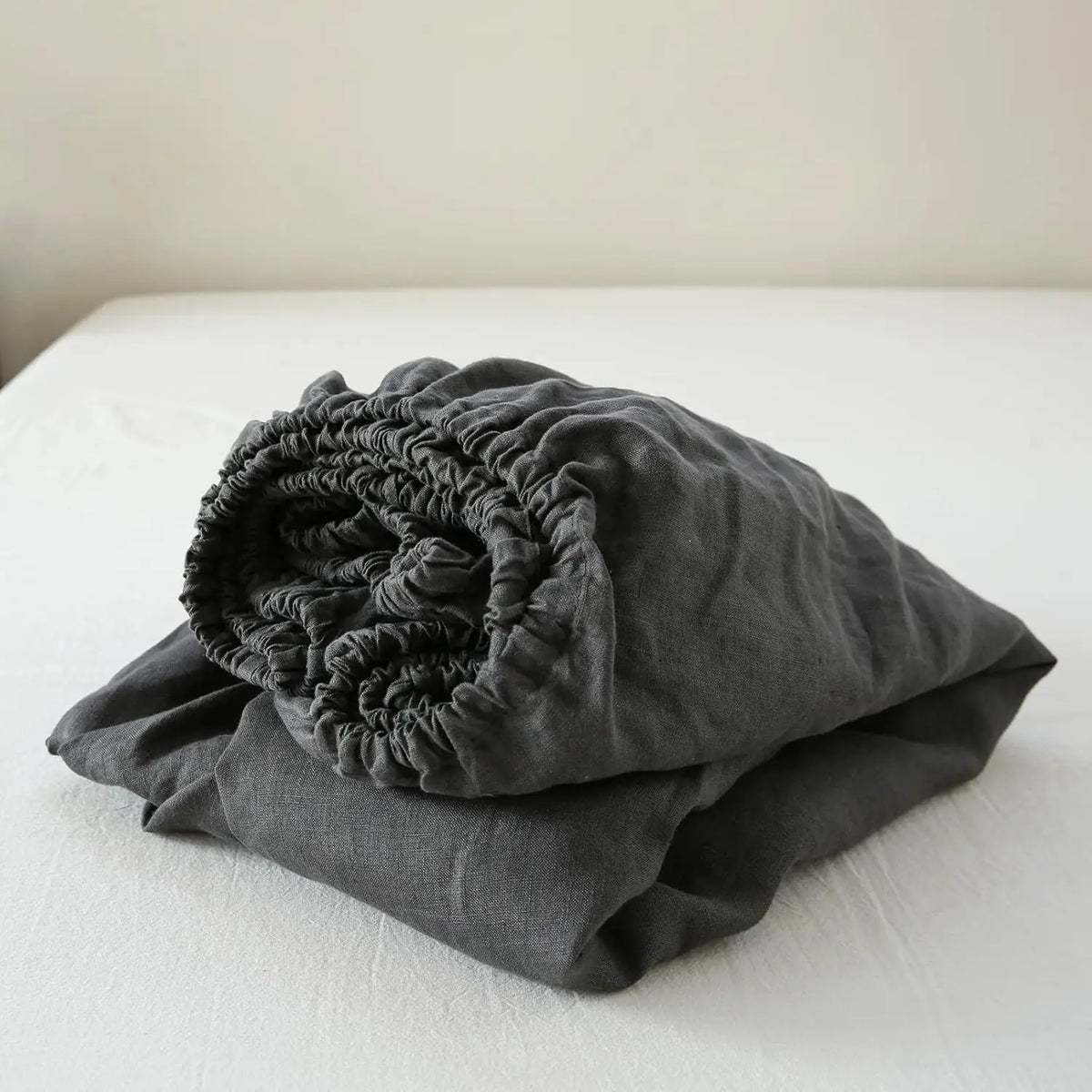 A dark gray linen fitted sheet with deep pockets is folded on a white surface.