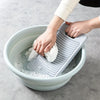 A hand is using a non-slip plastic laundry scrubbing board inside a light blue basin to clean stains.
