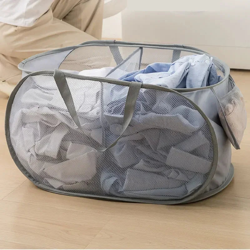 A gray folding mesh laundry basket with handles filled with light blue and white clothing.