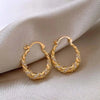 Gold twisted zircon hoop earrings displayed on a neutral fabric background