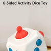 A white, six-sided activity dice toy with red and blue accents is shown on a wooden surface.