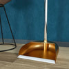 A modern brass broom and dustpan set with a floor wiper resting on a wooden surface.