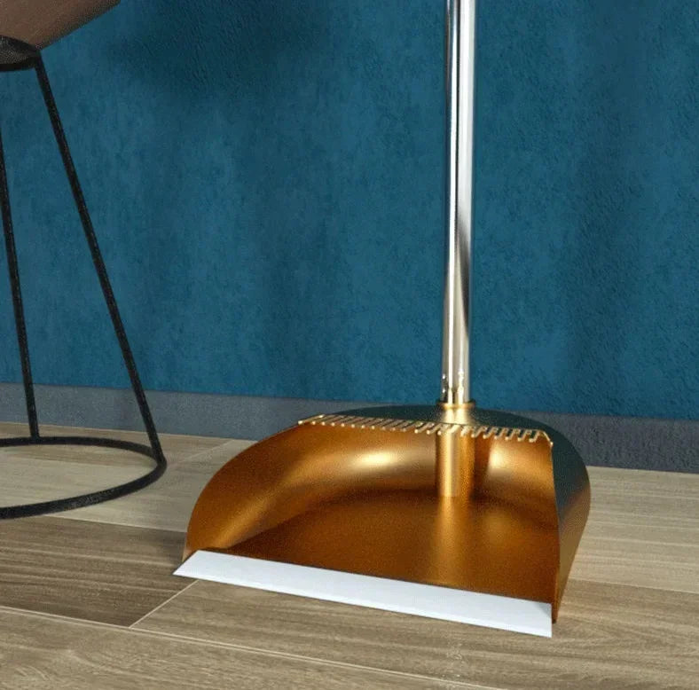 A modern brass broom and dustpan set with a floor wiper resting on a wooden surface.