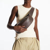 Model in cream top and beige trousers holding a brown leather crossbody bag