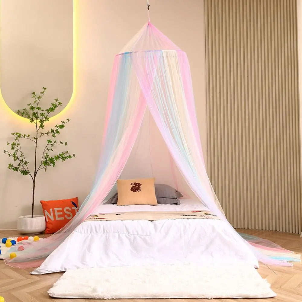 A white bed decorated with a rainbow hanging dome canopy mosquito net and pillows in a light room.