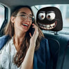 A woman smiling while using a phone in a car, with a black smiley face headrest cushion cover visible.