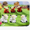 A collection of adorable resin Highland cow figurines in orange and white colors displayed on green grass.