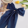 A navy blue silk bow hair clip and ponytail holder next to yellow tulips and a magazine.
