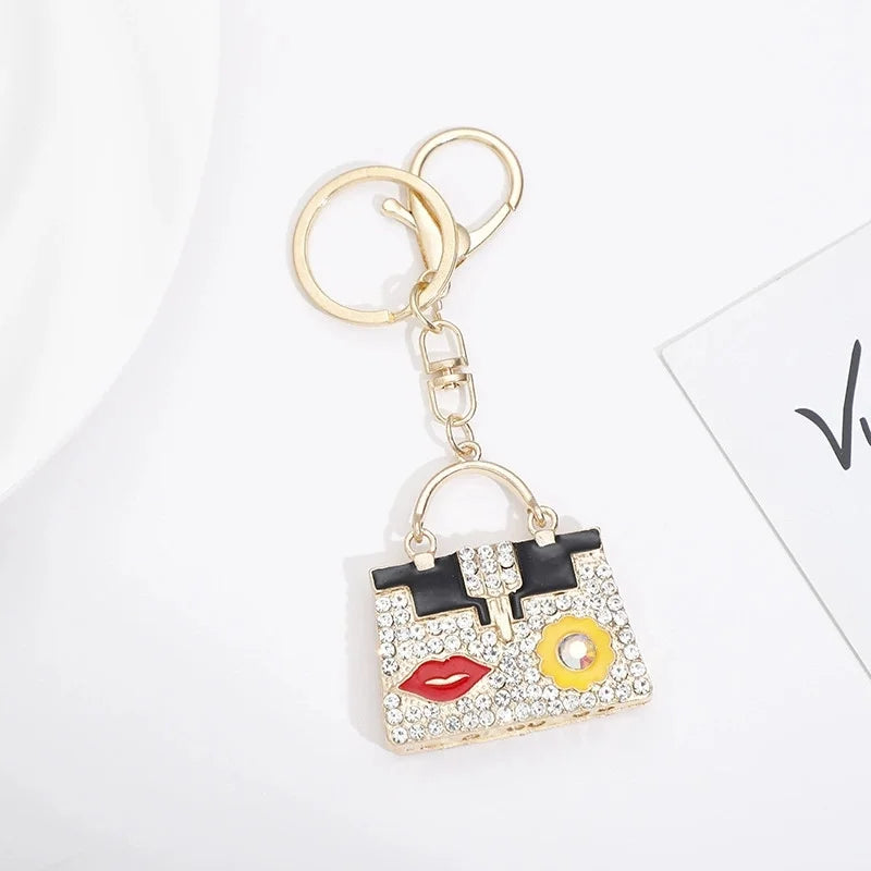 Gold chain keychain featuring a square handbag charm decorated with black and gold patterns and colorful rhinestones