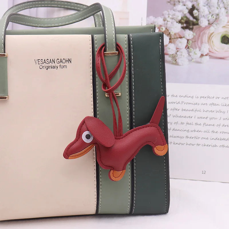 A light beige and olive green PU leather handbag with a red dachshund keychain charm.