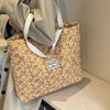 A beige corduroy tote bag with a floral pattern is held by a person in a light-colored coat.