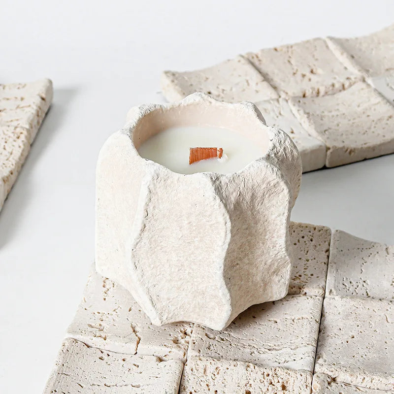 A white silicone mold shaped like a wavy edge container holding a lit candle inside.