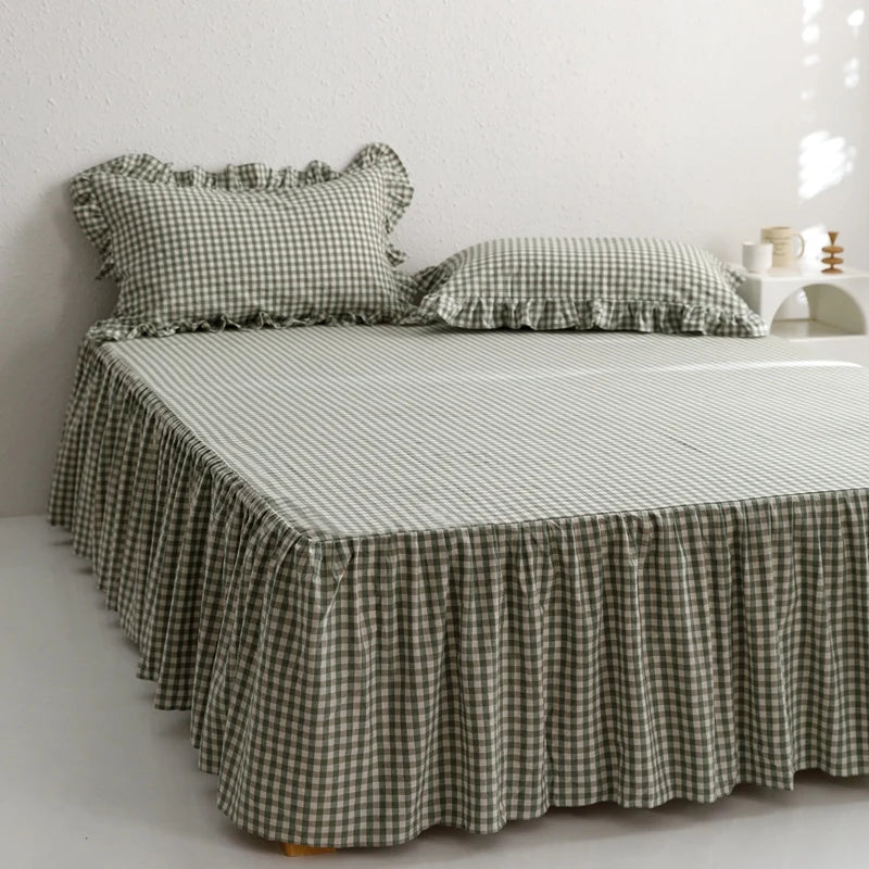 A bed featuring a plaid fabric bed skirt and pillows on a white background.