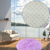 A fluffy purple shaggy round rug placed on a wooden floor in a modern living space overlooking water.