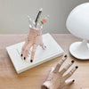 A pink resin Halloween hand planter and pen holder with small flowers and pens displayed on a white surface.