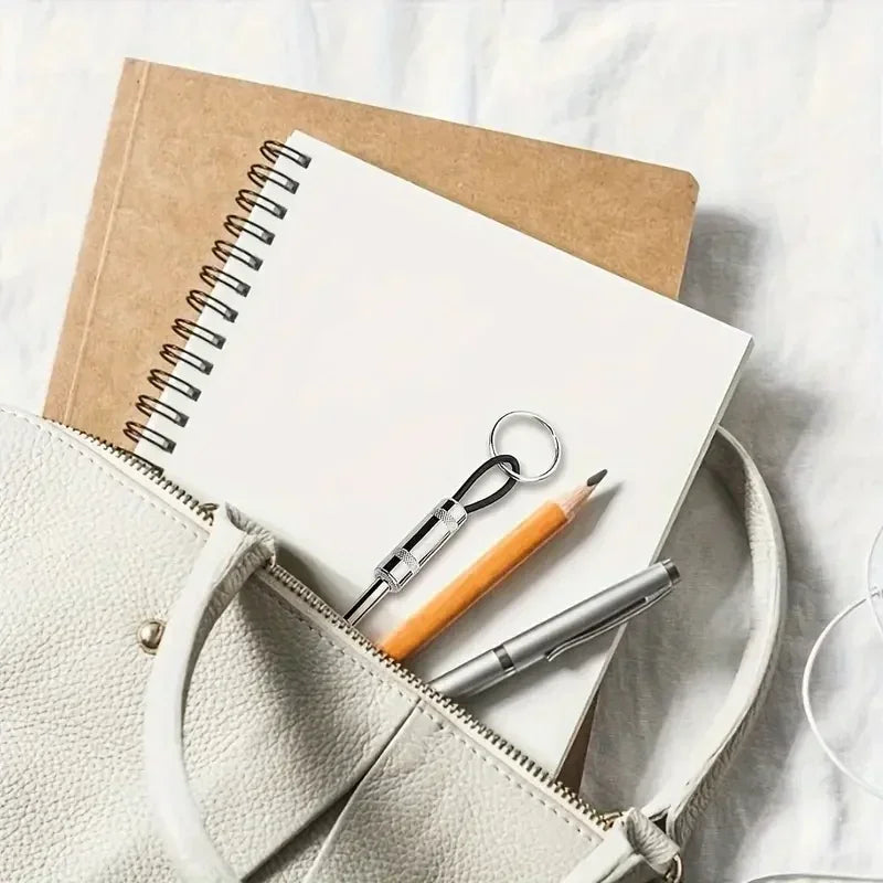 A beige leather bag holds a spiral notebook, a pencil, and a metal key holder on a white surface.