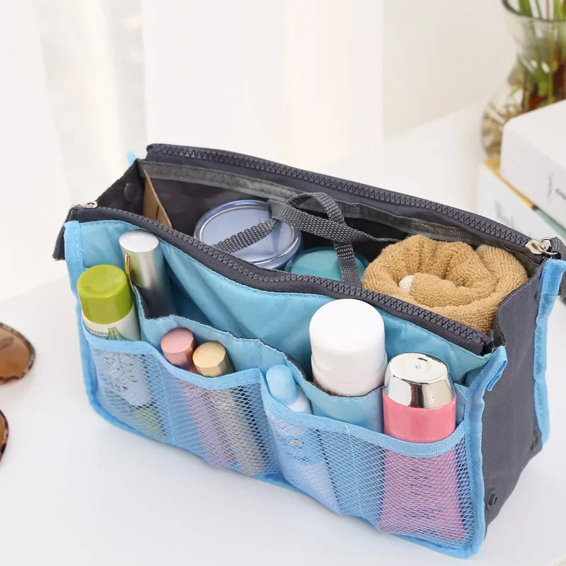 A blue foldable oxford cloth makeup organizer bag with multiple compartments and a mesh pocket is shown on a white surface.