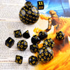 A collection of black polyhedral dice, including d4 through d12 and d20 shapes, laid out on a wooden surface.