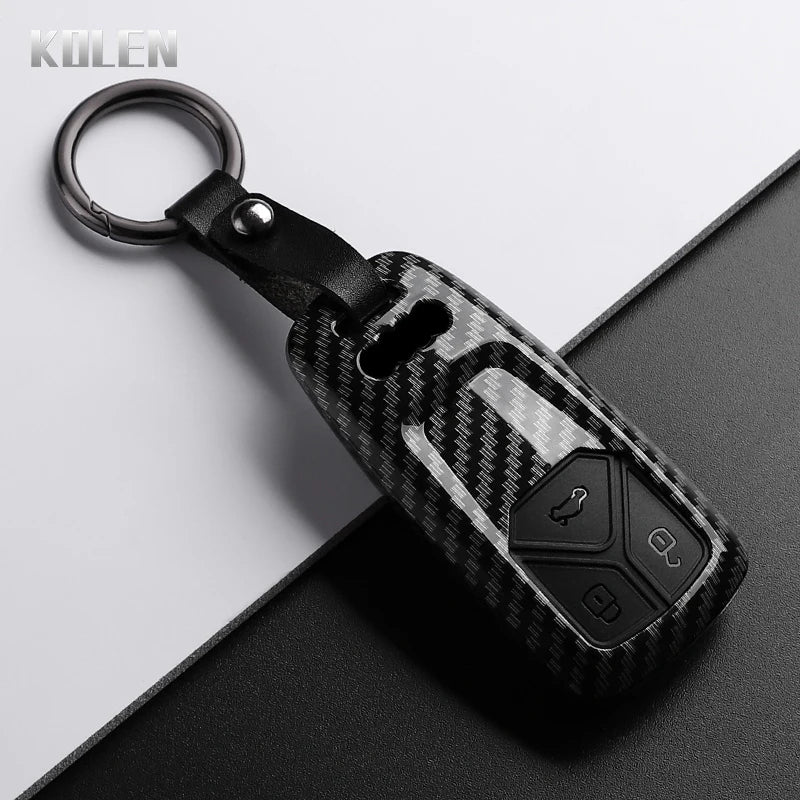 Black carbon fiber style key fob cover with a metal ring and black strap resting on a dark surface.