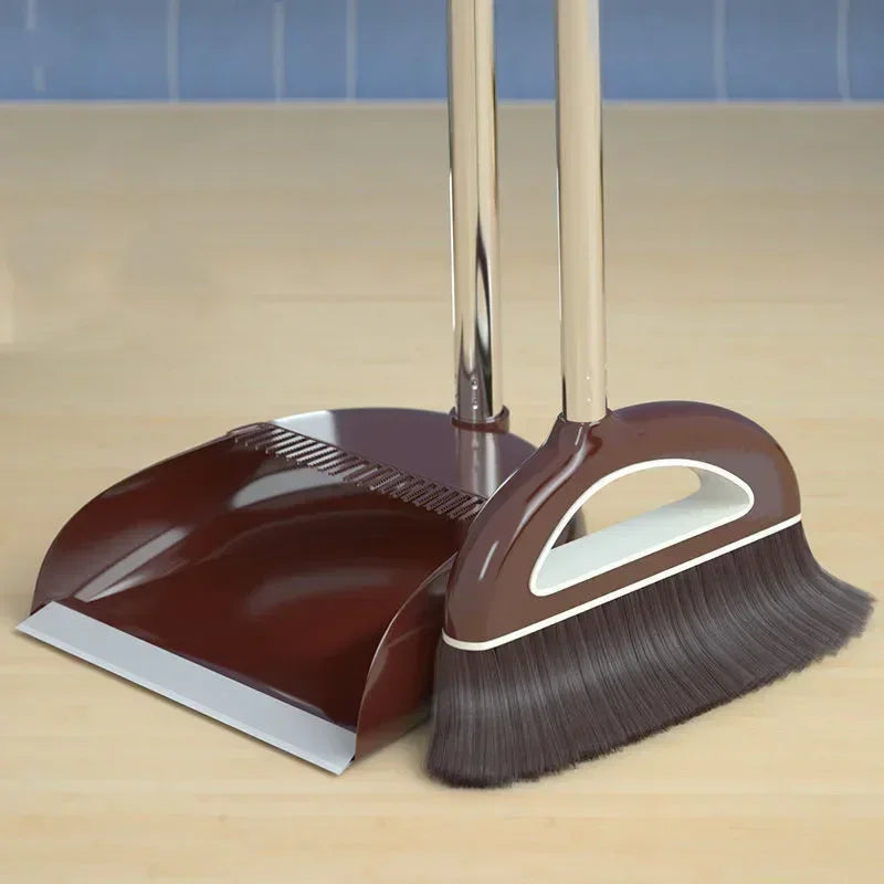 A brown broom and dustpan set with a floor wiper resting on a wooden surface.