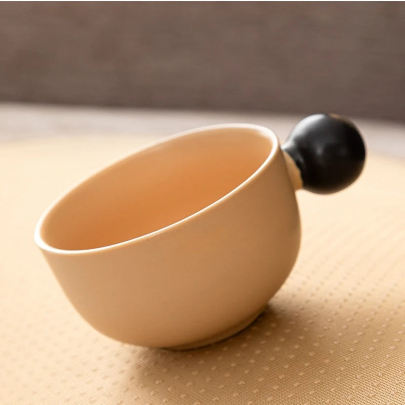 Una pequeña taza de cerámica beige con asa negra sobre una superficie amarilla texturizada.