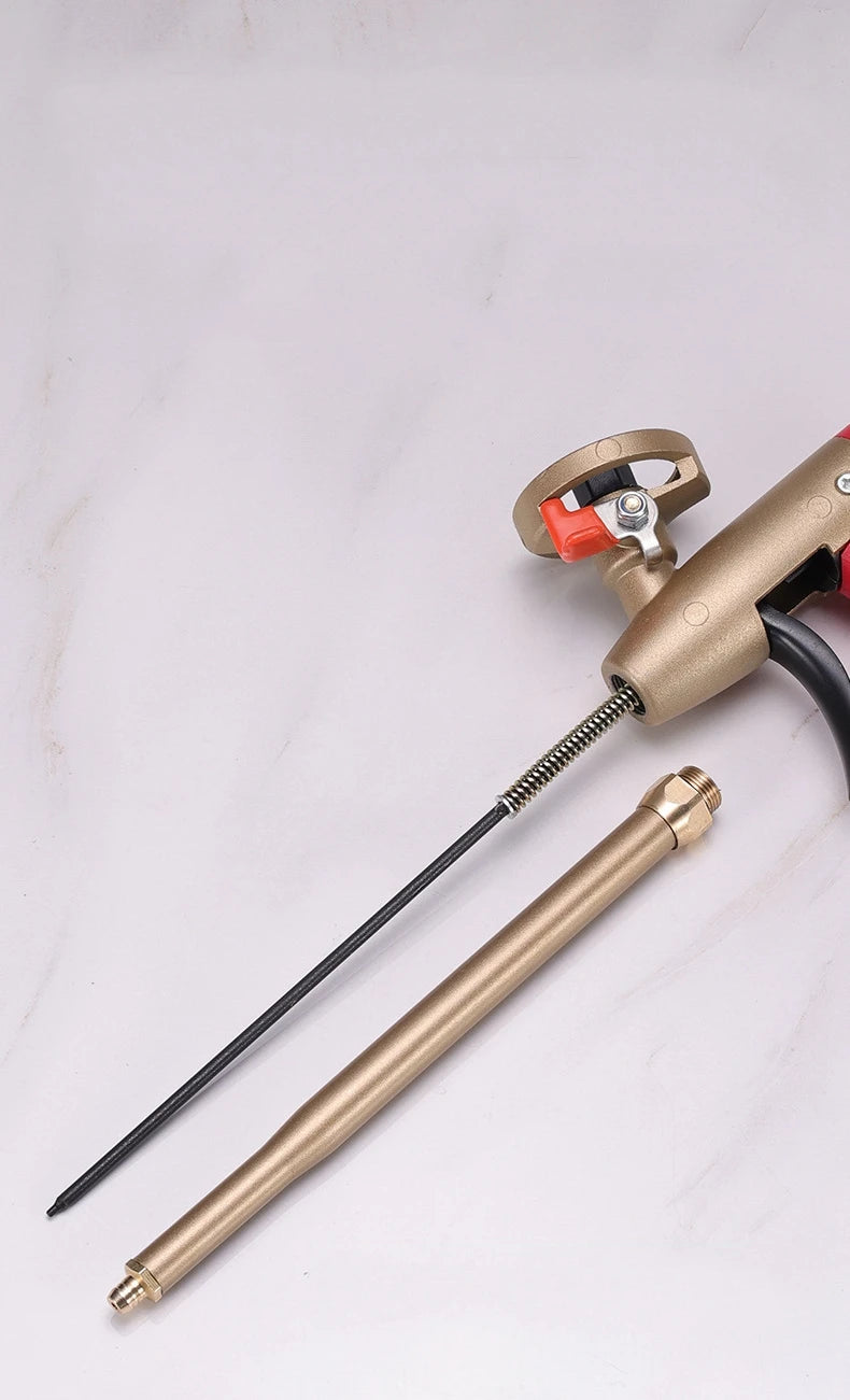 A close-up view of a brass adjustable foam spray gun with a black hose and nozzle on a white surface.