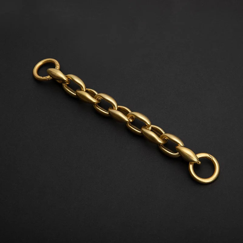A gold-colored acrylic chain strap for a handbag, laid diagonally on a dark surface.