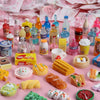 A collection of miniature resin food and drink figurines in various colors and shapes displayed on a pink background.