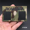 A rectangular camouflage patch with the word ROMANIA on a green and brown pattern is held in a hand.